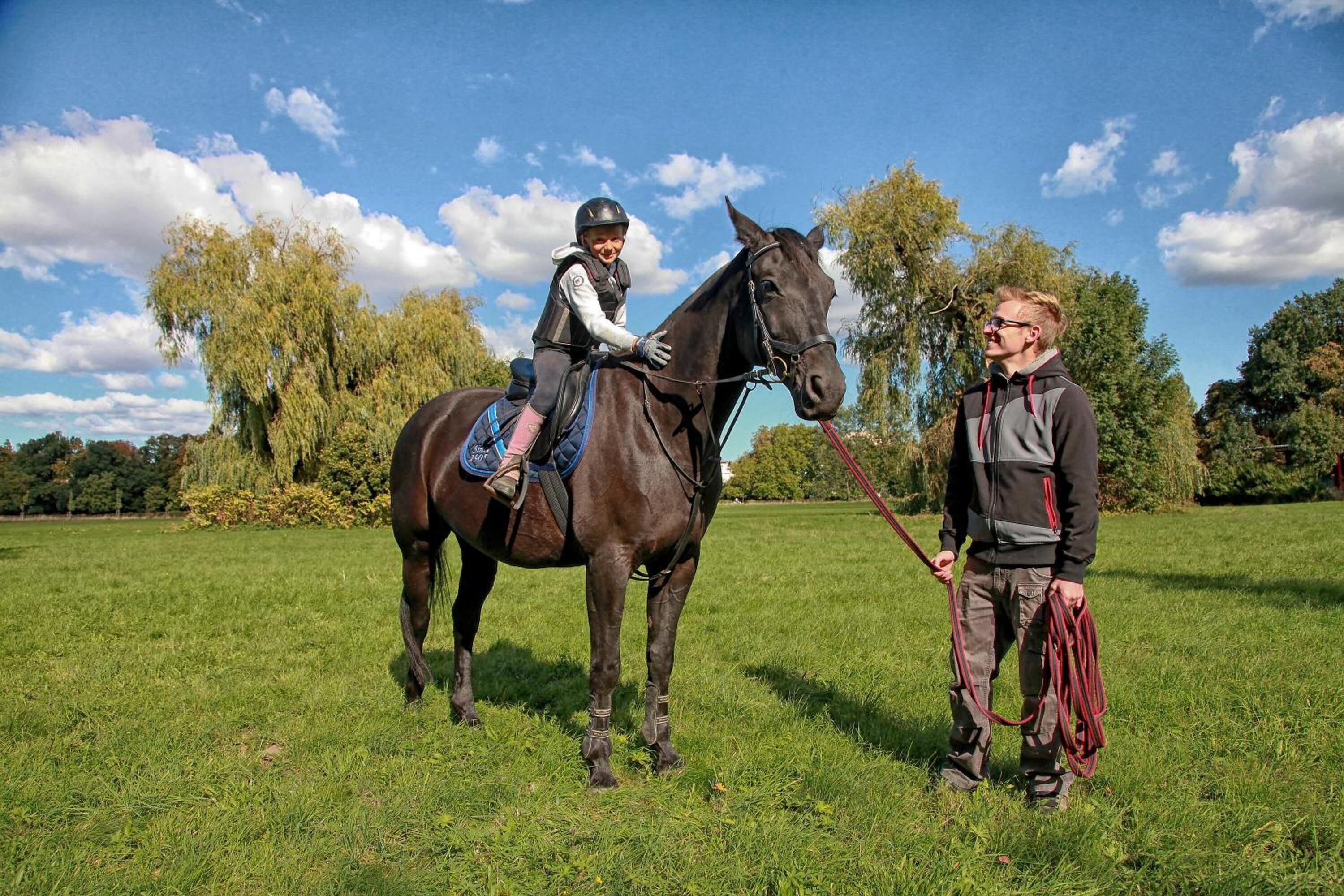 A person on a horse in a grassy field with trees in the background.