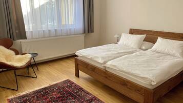 Quarto com cama de madeira, tapete vermelho estampado, uma cadeira e janela com cortinas.