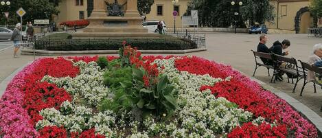 A public square with a statue, flower beds, and a building with a red roof.