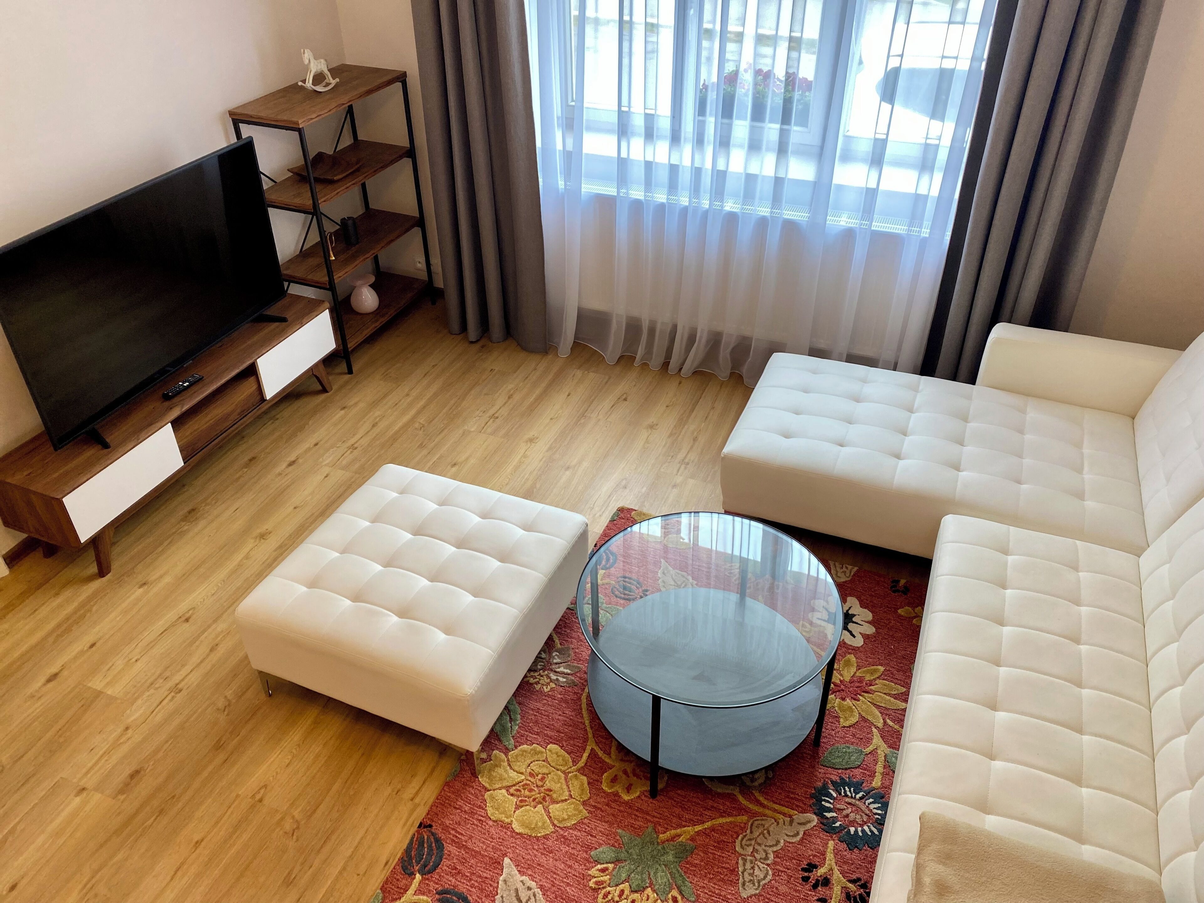 Ein Wohnzimmer mit Fernseher, Sofa, Hocker und Glastisch.
