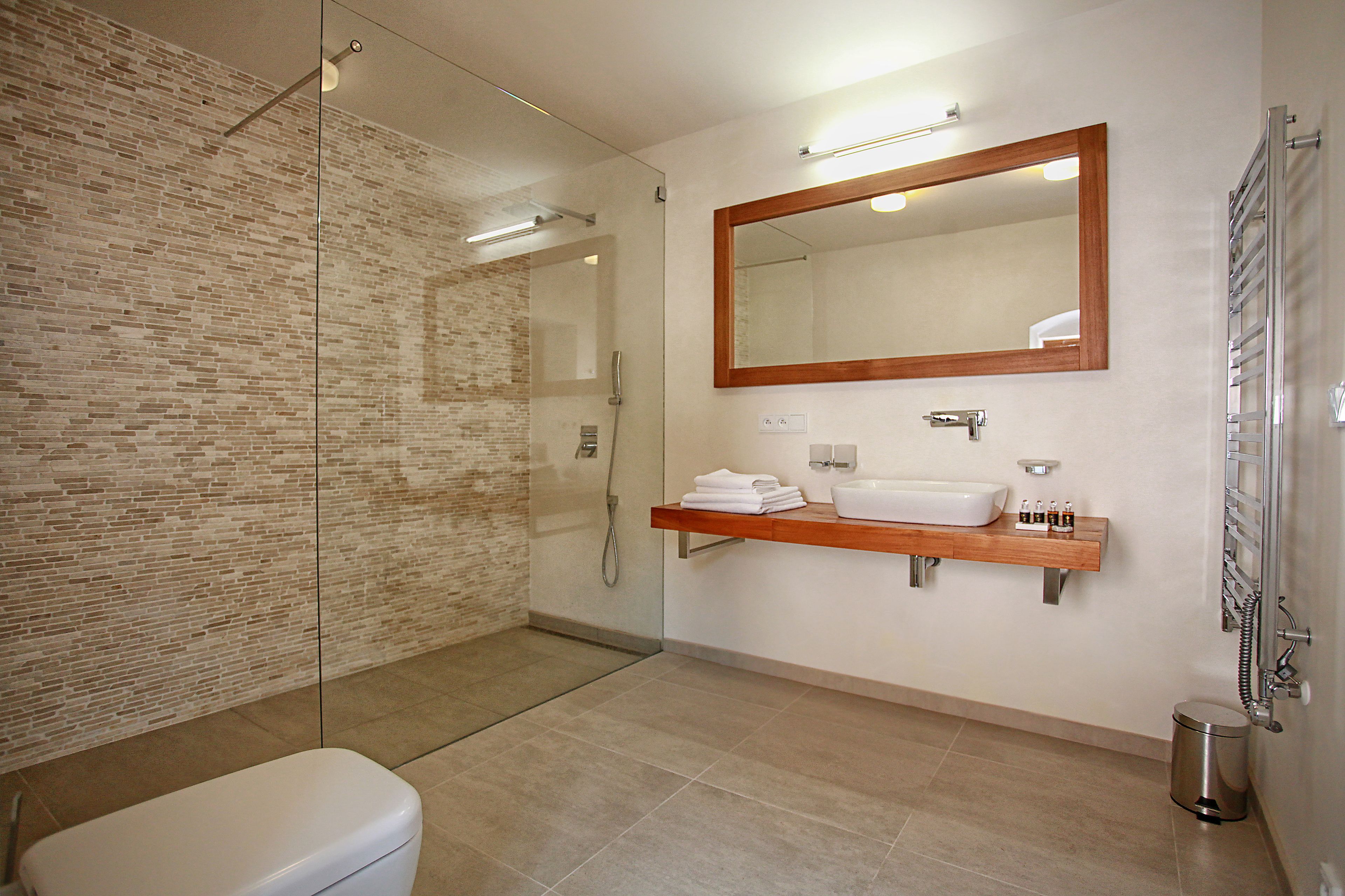 Ein modernes Badezimmer mit Duschkabine aus Glas, einem Holzkosmetikschrank mit Waschbecken und Spiegel sowie einer Toilette.