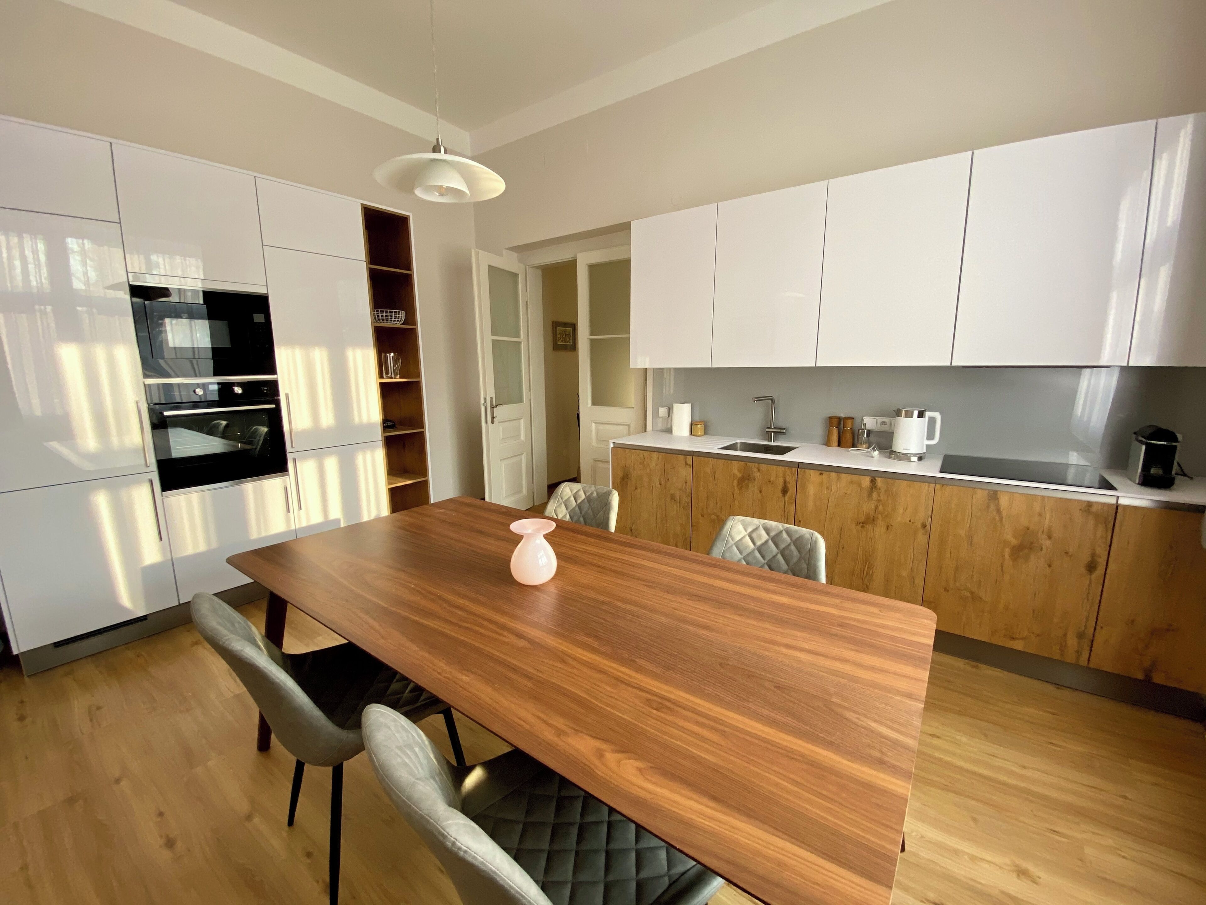 A modern kitchen with white cabinets, a wooden dining table, and a built-in oven.