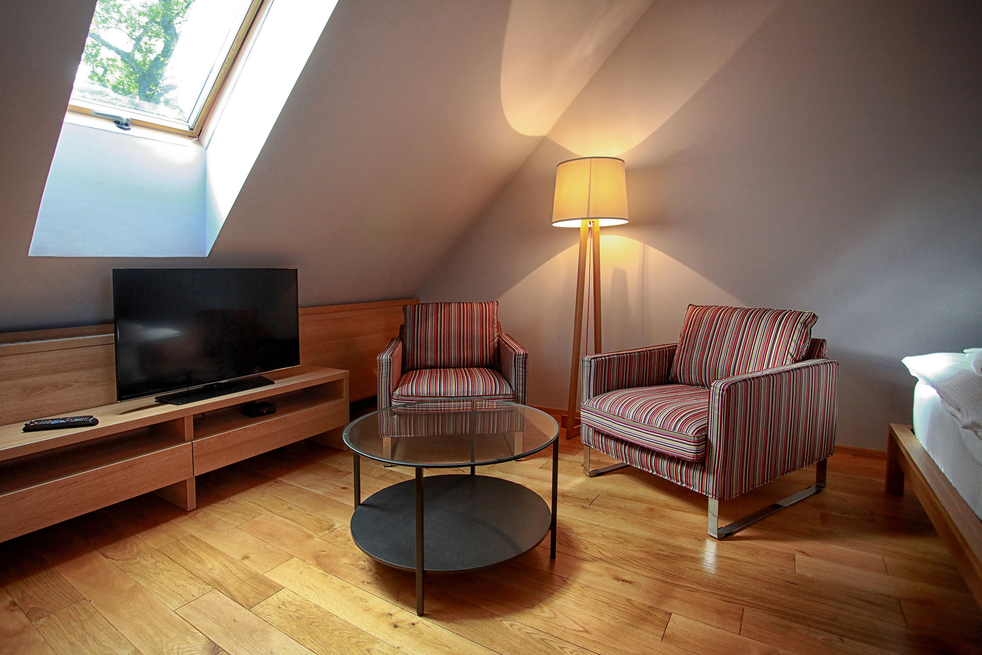 Una habitación moderna con televisión, dos sillones a rayas, una mesa de centro de vidrio y una lámpara de pie.