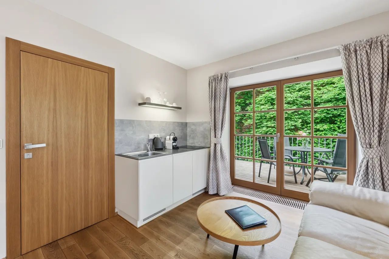 A compact kitchen with a built-in stove, a dining area with a round table, and a large window with a view of greenery.