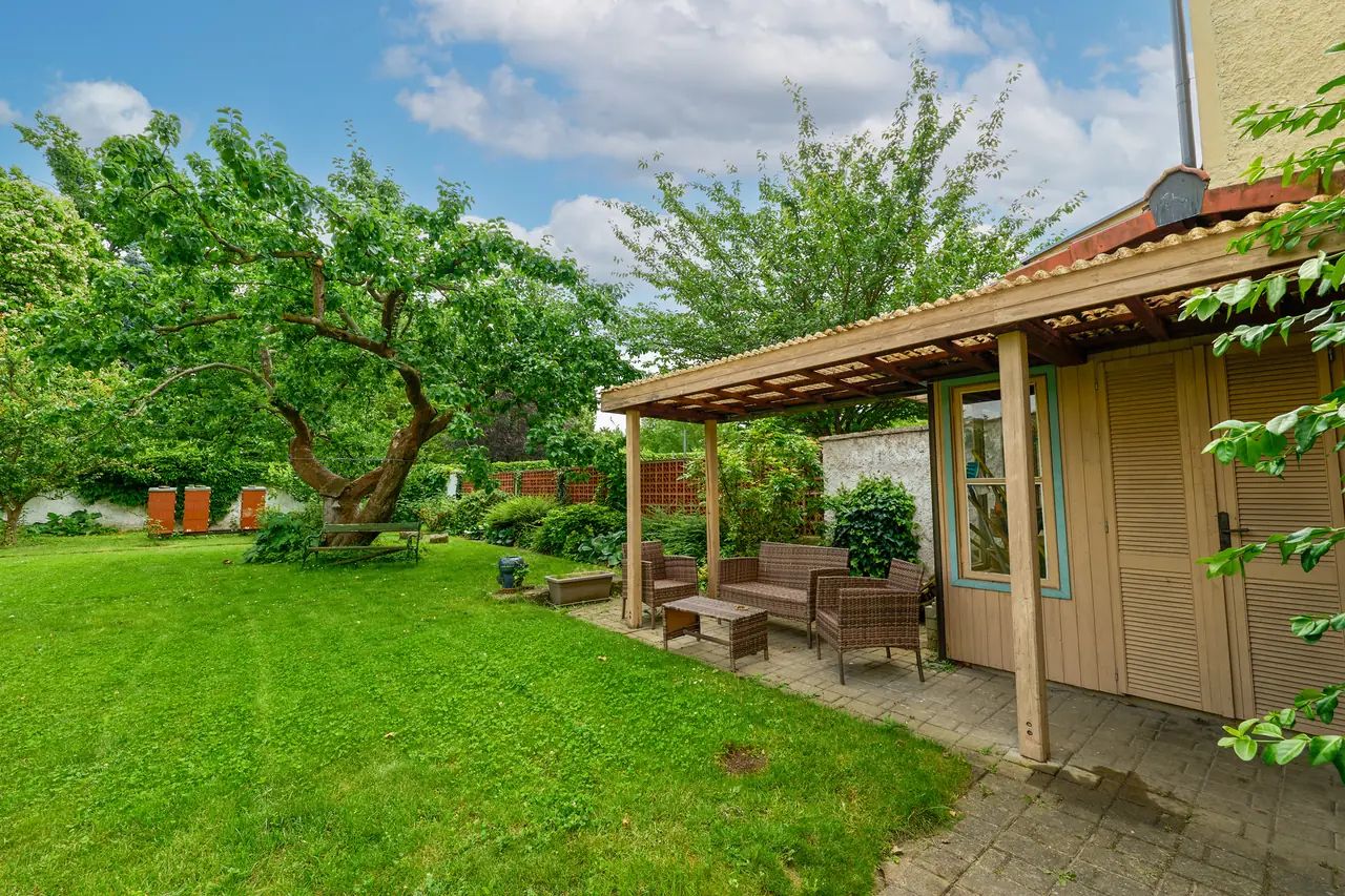 Eine Terrasse mit Gartenmöbeln, einer Pergola und Blick auf einen üppigen Garten.