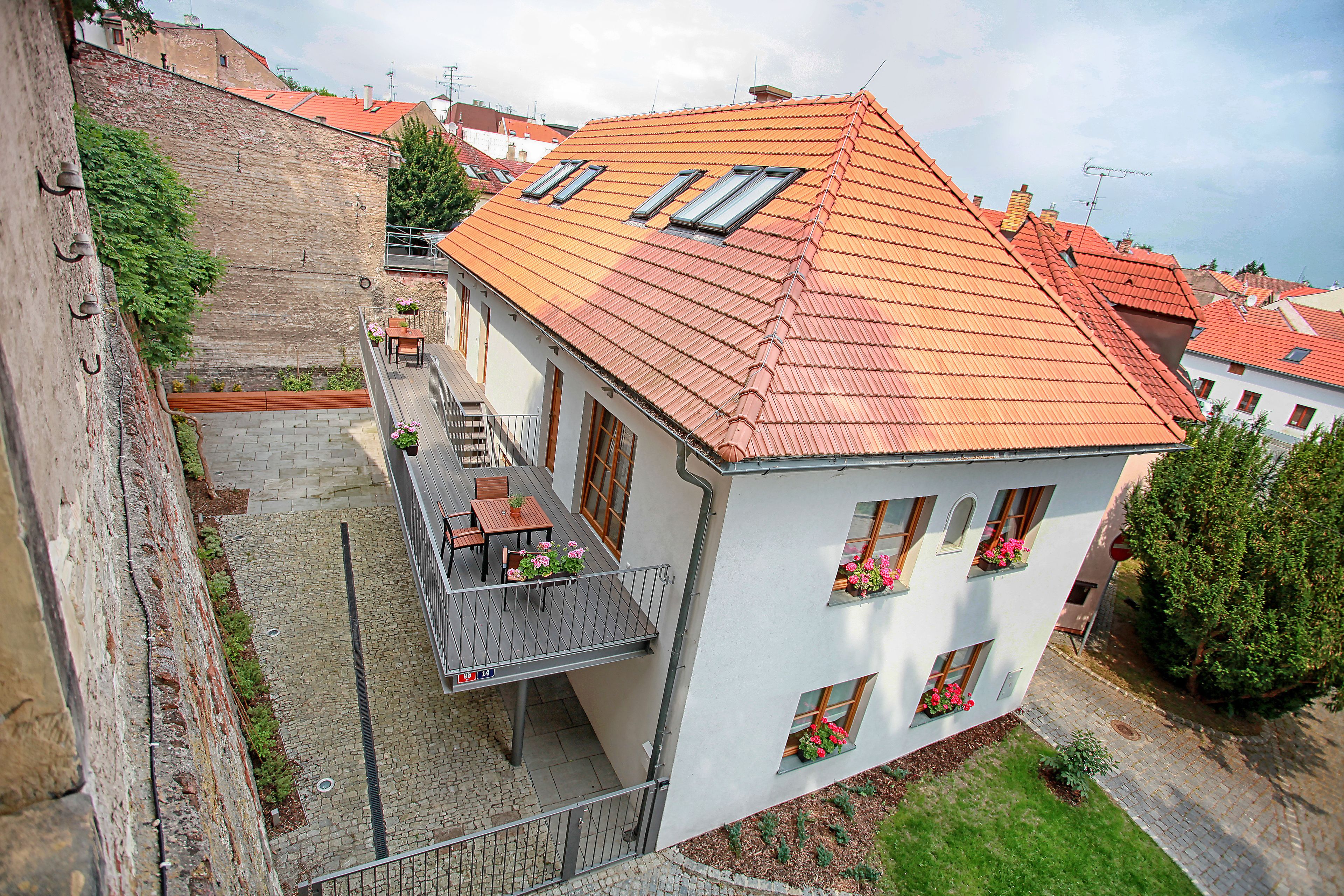A two-story building with a red-tiled roof, a balcony with outdoor furniture, and flower boxes on the windows.