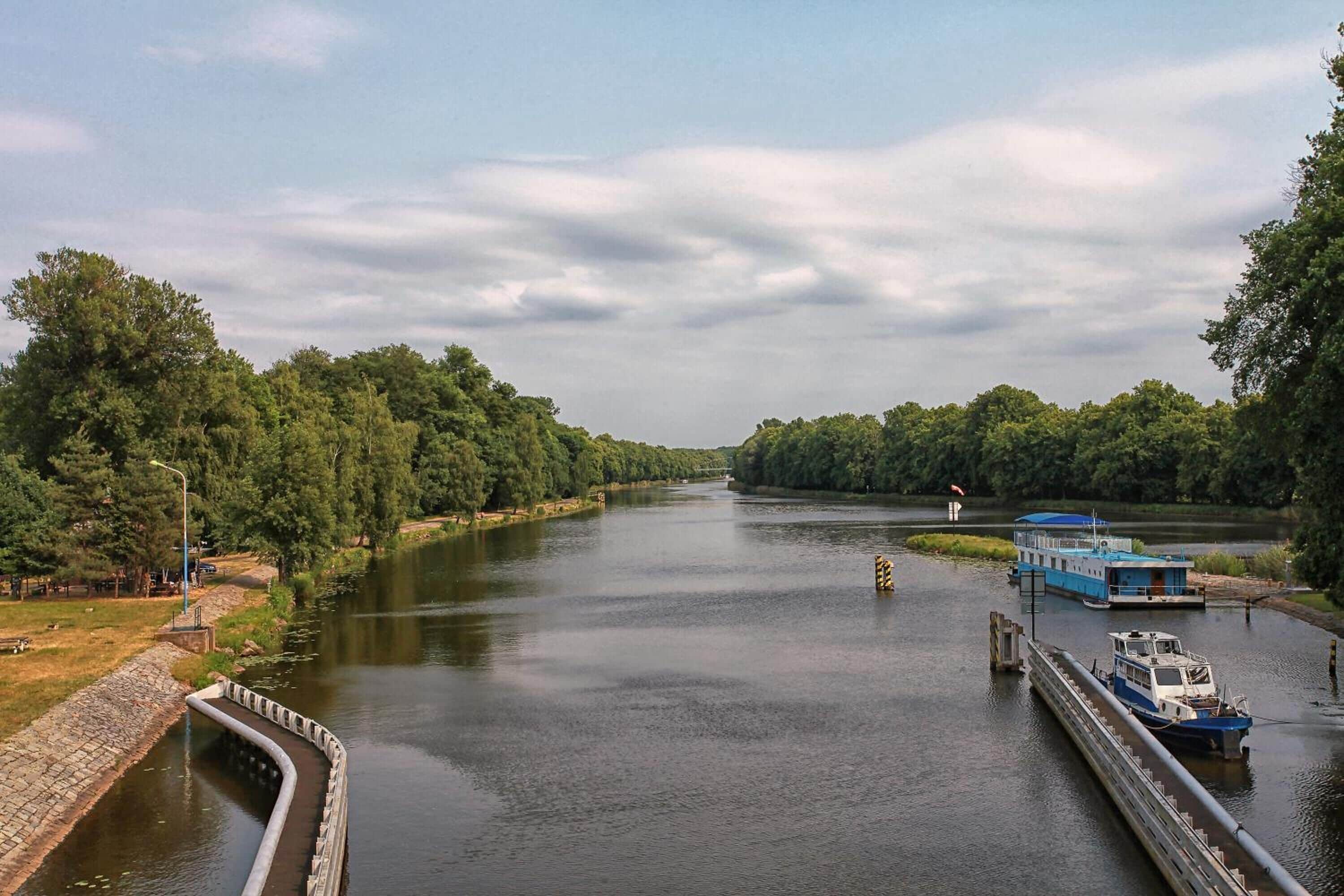 Un río con esclusas, una embarcación azul amarrada y un puente al fondo.