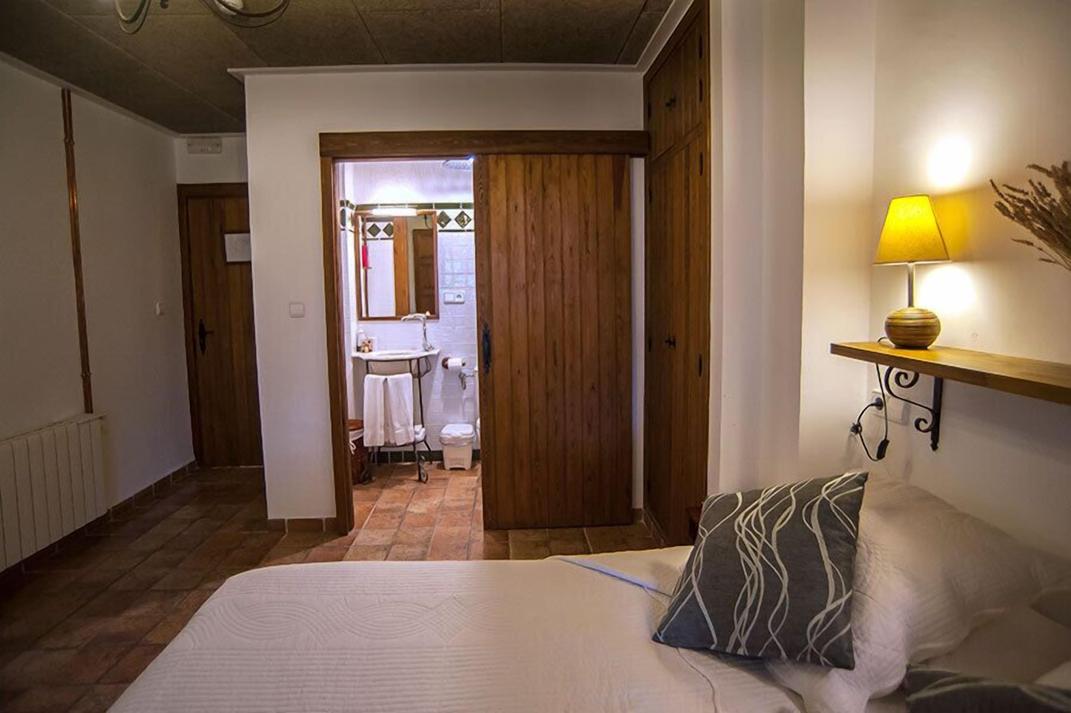 A bedroom with a bed, a bedside lamp, and a view into the bathroom.