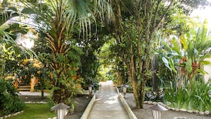 A pathway flanked by lush greenery and stone lanterns, leading through a tropical garden. - Pousada Bemvirá (Porto Seguro)