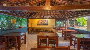 A restaurant with wooden tables and chairs, a tiled floor, and a thatched roof. - Pousada Bemvirá (Porto Seguro)