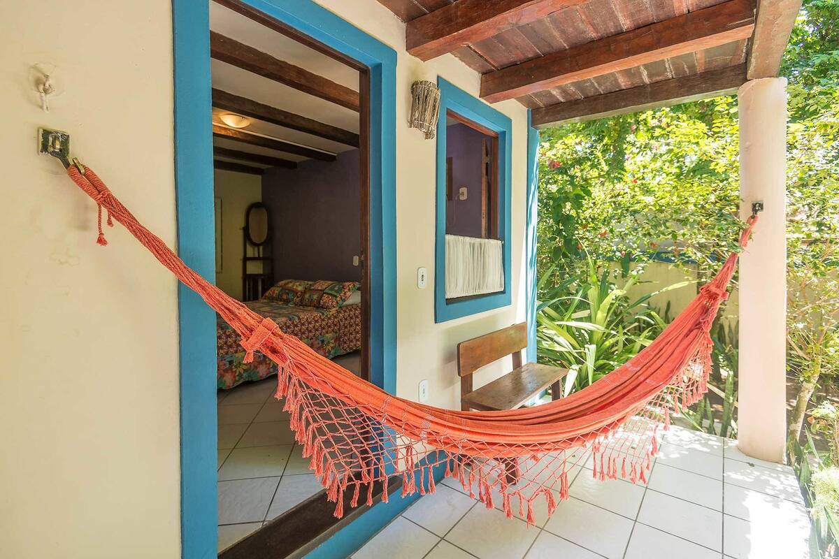 A hammock tied between two pillars in a room with a tiled floor and a view of greenery outside.