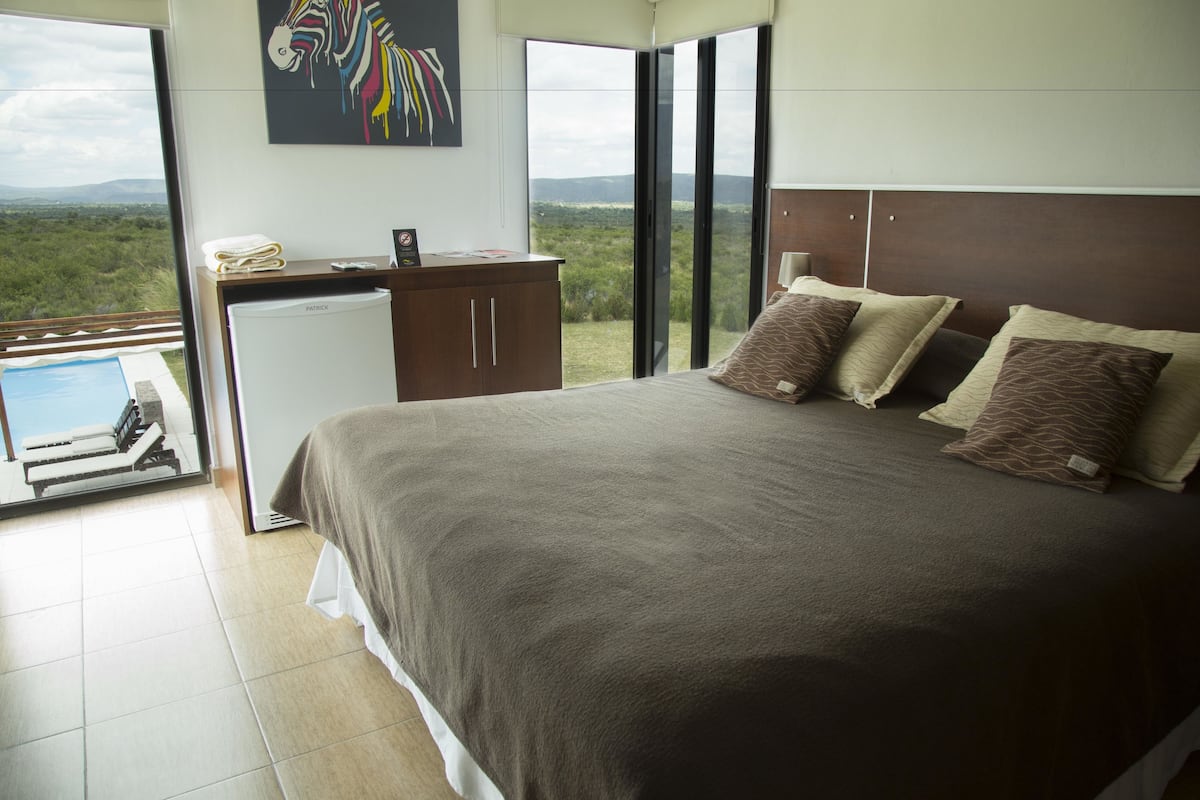 Een slaapkamer met een groot bed, een bureau met een computer en uitzicht op het landschap.