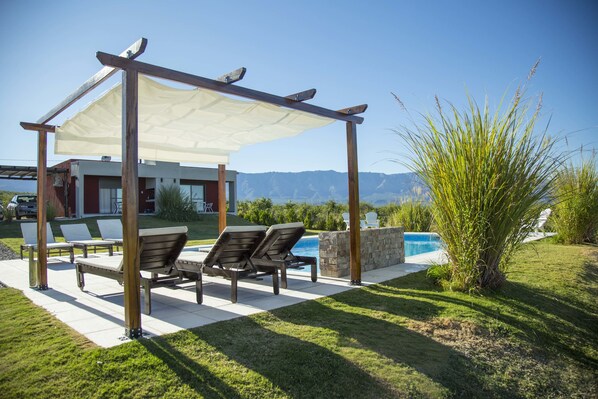 Un patio con mobiliario exterior, piscina y vistas a montañas.