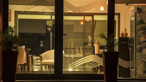 Een hotel receptie met een glazen deur, plantenbakken, een zithoek met een stoel en een koelkast van Heineken.
