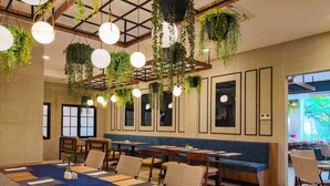 Un restaurante con una larga mesa compartida, cabinas, plantas colgantes y obras enmarcadas en las paredes.