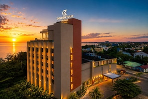 A hotel with a modern design, a prominent sign, and a view of the sunset over the water. - Golden Tulip Belitung (Tanjung Pandan)
