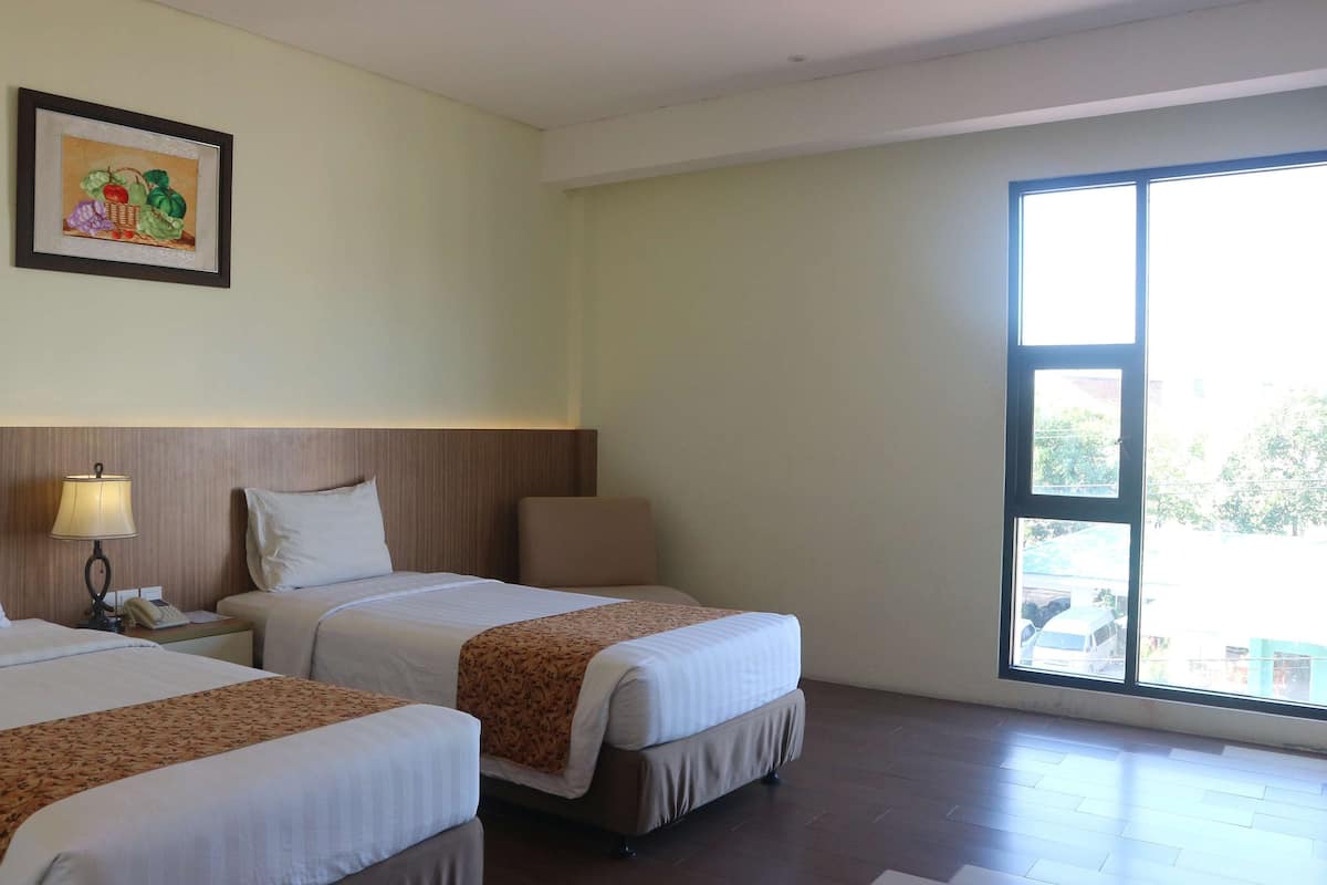 A hotel room with two beds, a nightstand with a lamp, a framed picture on the wall, and a large window with a view of the outside.