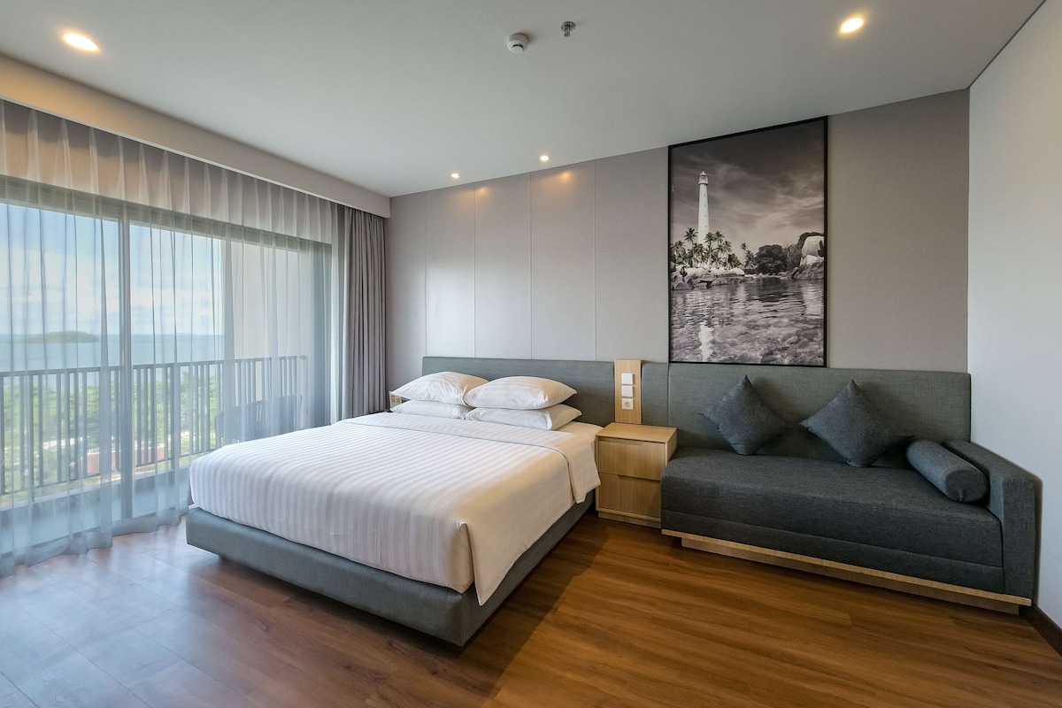 Una camera da letto moderna con un letto grande, un divano, un comodino e un quadro raffigurante un faro.
