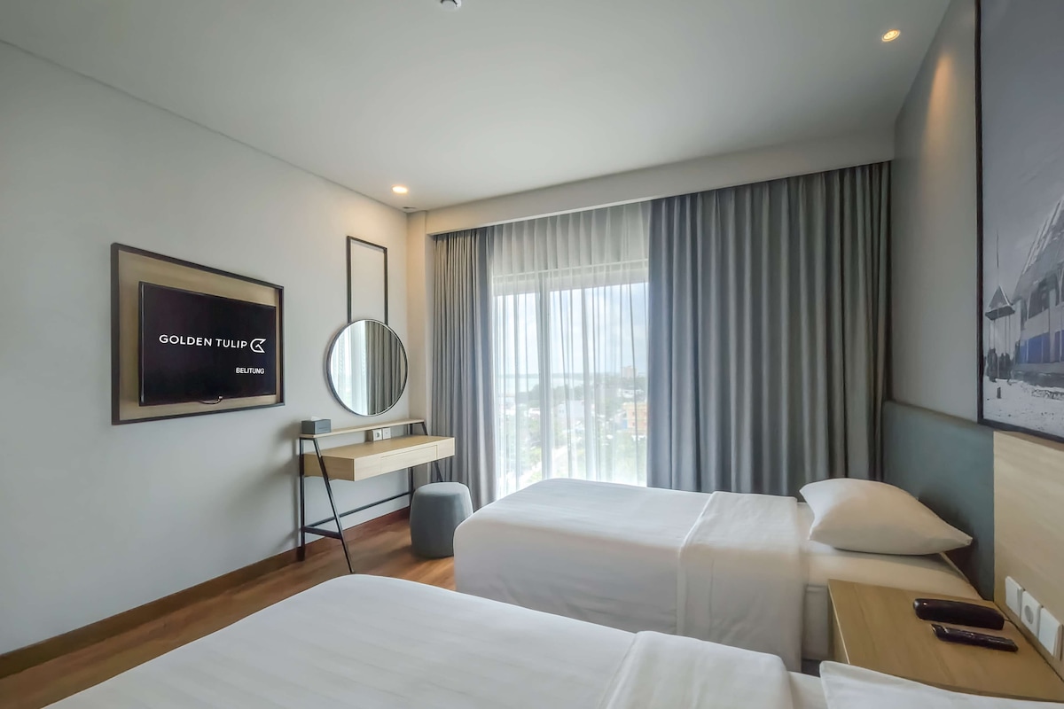 Een hotelkamer met twee bedden, een televisie, een spiegel en een raam met gordijnen.