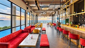 Un restaurant moderne avec des sièges rouges, un bar et de grandes fenêtres donnant sur la mer.
