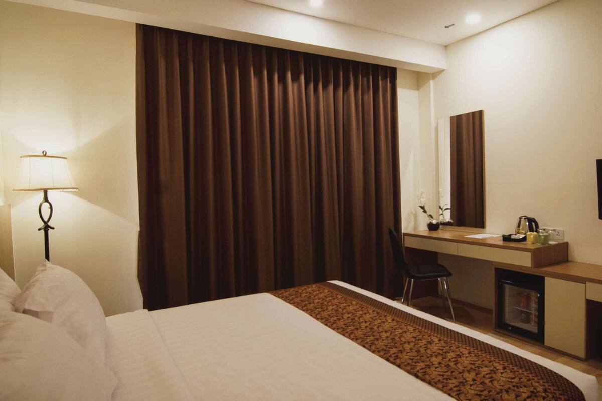 A hotel room with a bed, a desk, a chair, a television, and a large window with curtains.