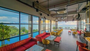 Un espacio interior amplio con ventanas grandes, asientos rojos, sillas amarillas y vista al mar.