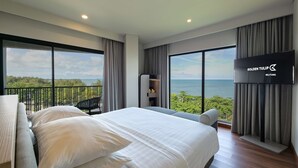 Habitación de hotel con una cama grande, un televisor en la pared y un balcón con vistas al mar.