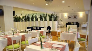 Un comedor con mesas dispuestas para una comida, sillas con cojines y un arreglo floral decorativo.