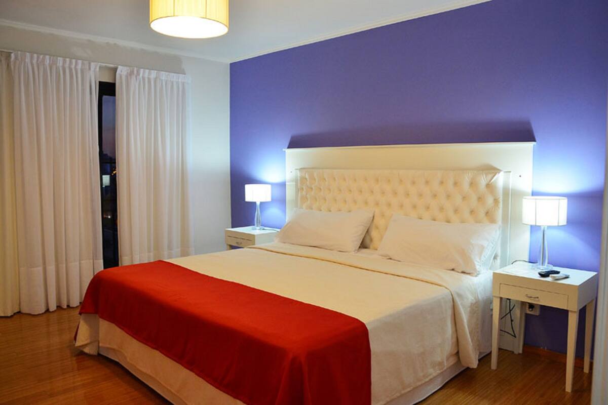 A neatly made bed with a red bedspread, two bedside lamps, and a white nightstand.