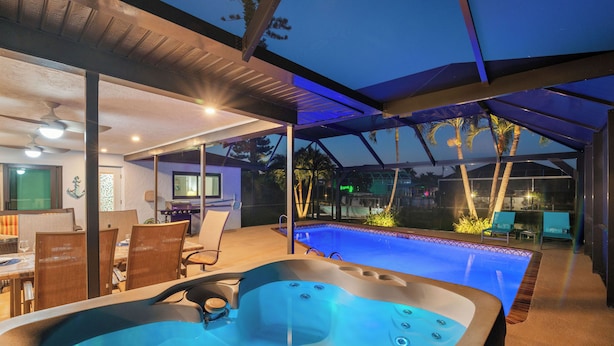 A modern outdoor pool area with a hot tub, covered seating, and a dining area. - Villa Turquoise Coast (Cape Coral)