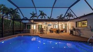 A swimming pool with a covered patio area, outdoor seating, and a view of palm trees. - Villa Turquoise Coast (Cape Coral)