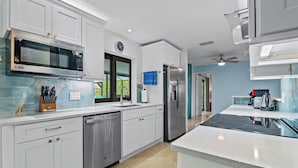 A modern kitchen with white cabinetry, stainless steel appliances, and a large window. - Villa Turquoise Coast (Cape Coral)