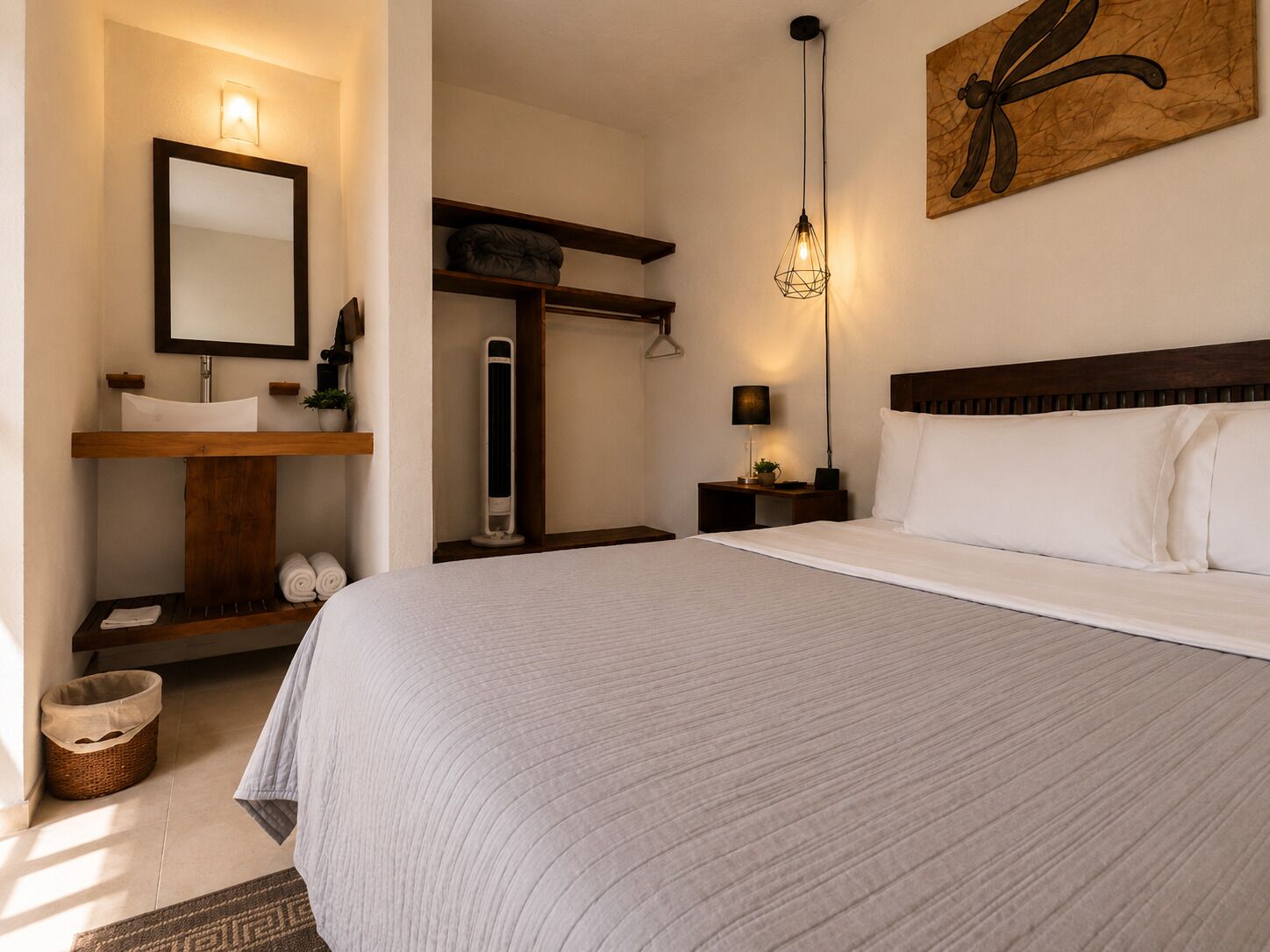 Una camera da letto con un letto, un comodino, uno specchio, uno scaffale con asciugamani, un'opera d'arte appesa al muro e una lampada a sospensione.