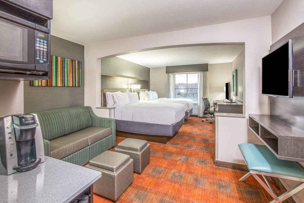 Habitación de hotel con cama, sofá, cafetera, televisor y microondas.