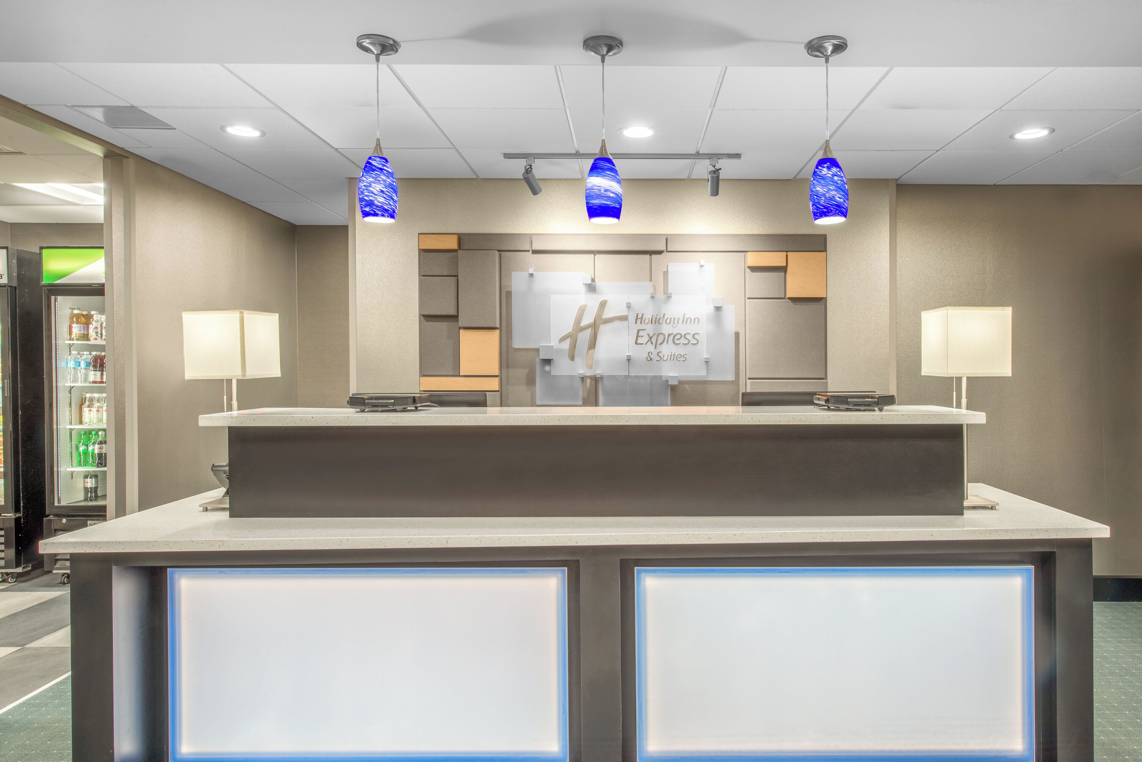 Een receptiebalie met een bordje Holiday Inn Express & Suites, verlichtingsarmaturen erboven en een automaat links.