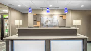 Un mostrador de recepción con un cartel de Holiday Inn Express & Suites, iluminación en el techo y una máquina expendedora a la izquierda.
