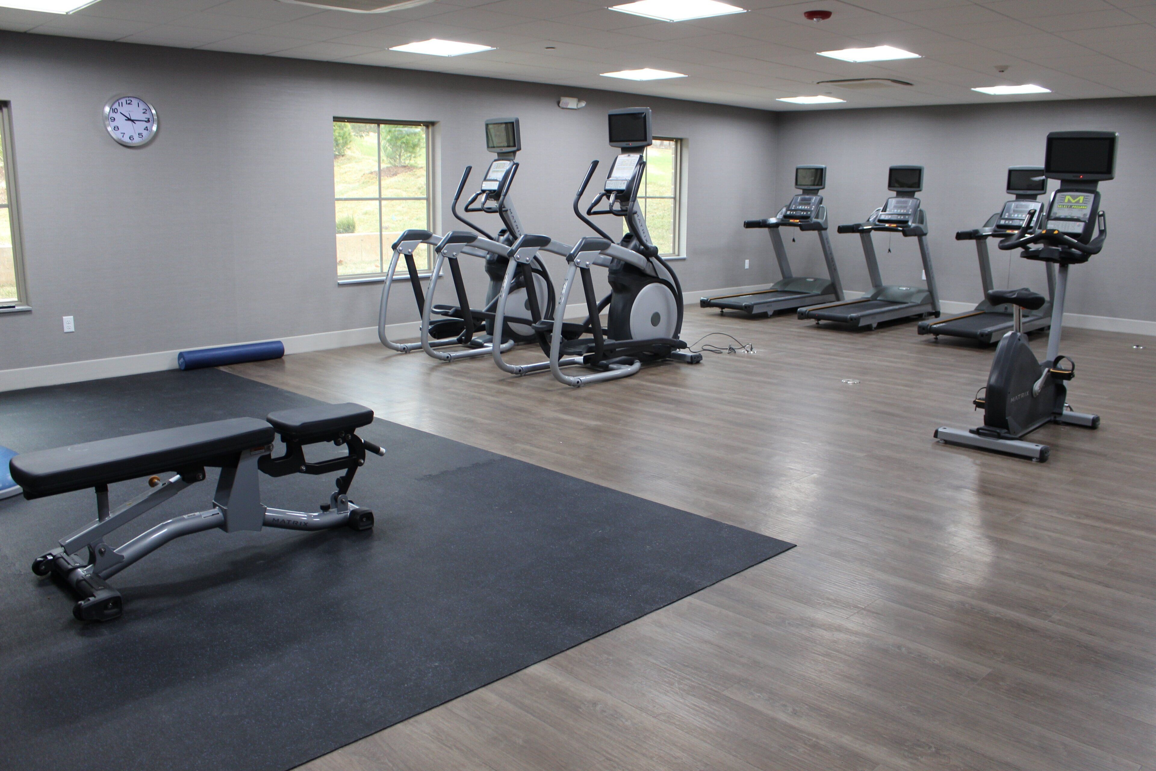 Une salle de sport équipée de tapis de course, de vélos elliptiques et d’un banc de musculation.