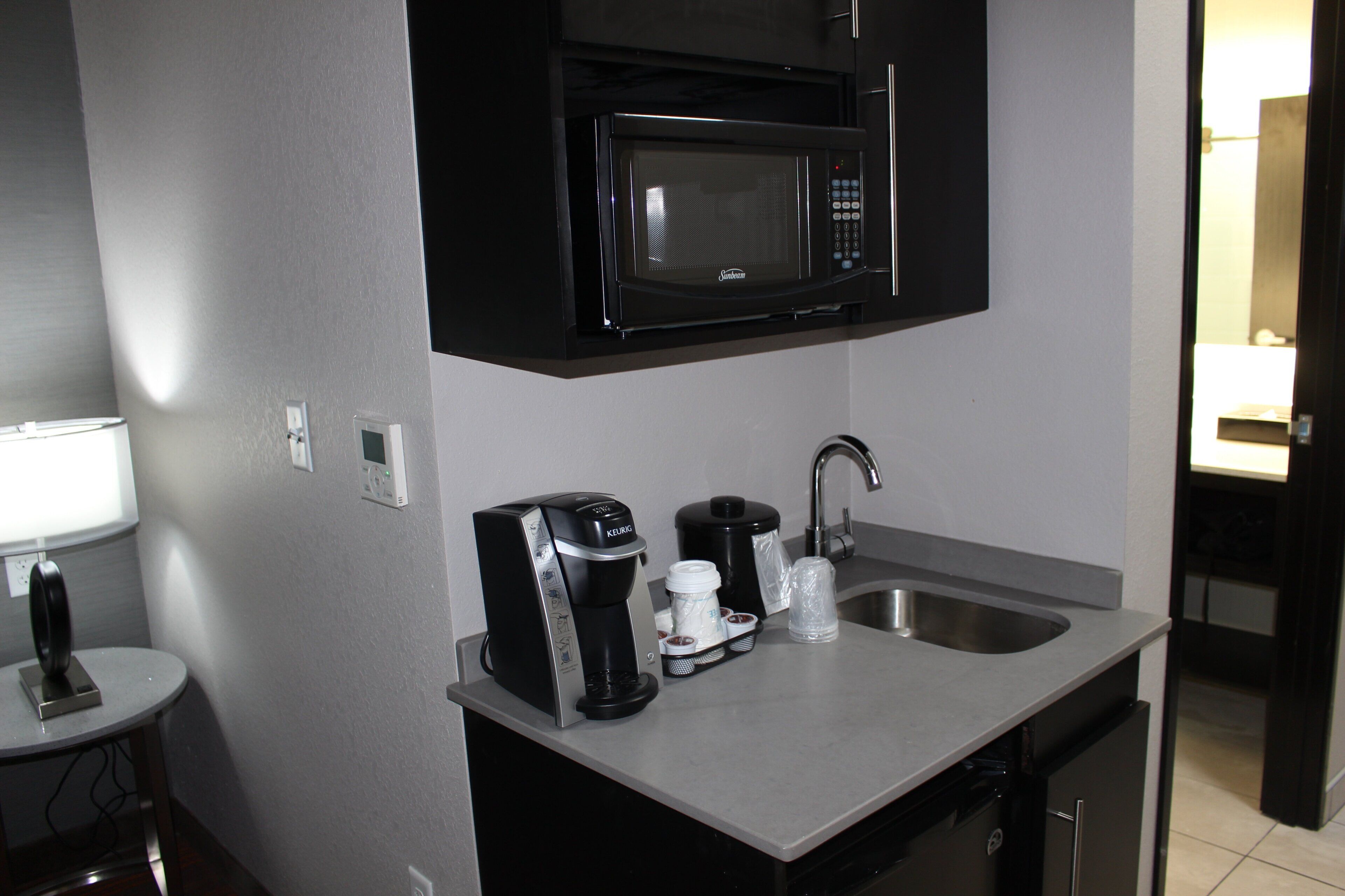 Una kitchenette compacta con microondas, cafetera y lavabo.