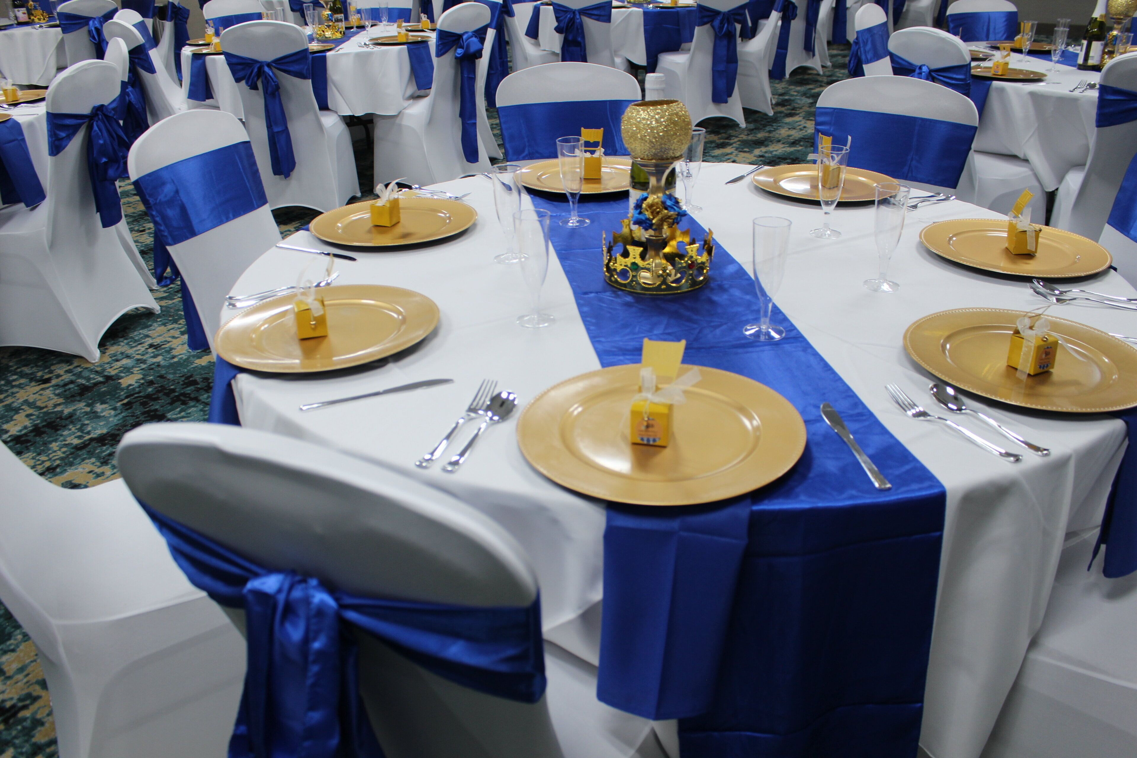 Un salón de banquetes con mesas redondas dispuestas para el servicio de comidas, cada una con platos y cubiertos dorados.