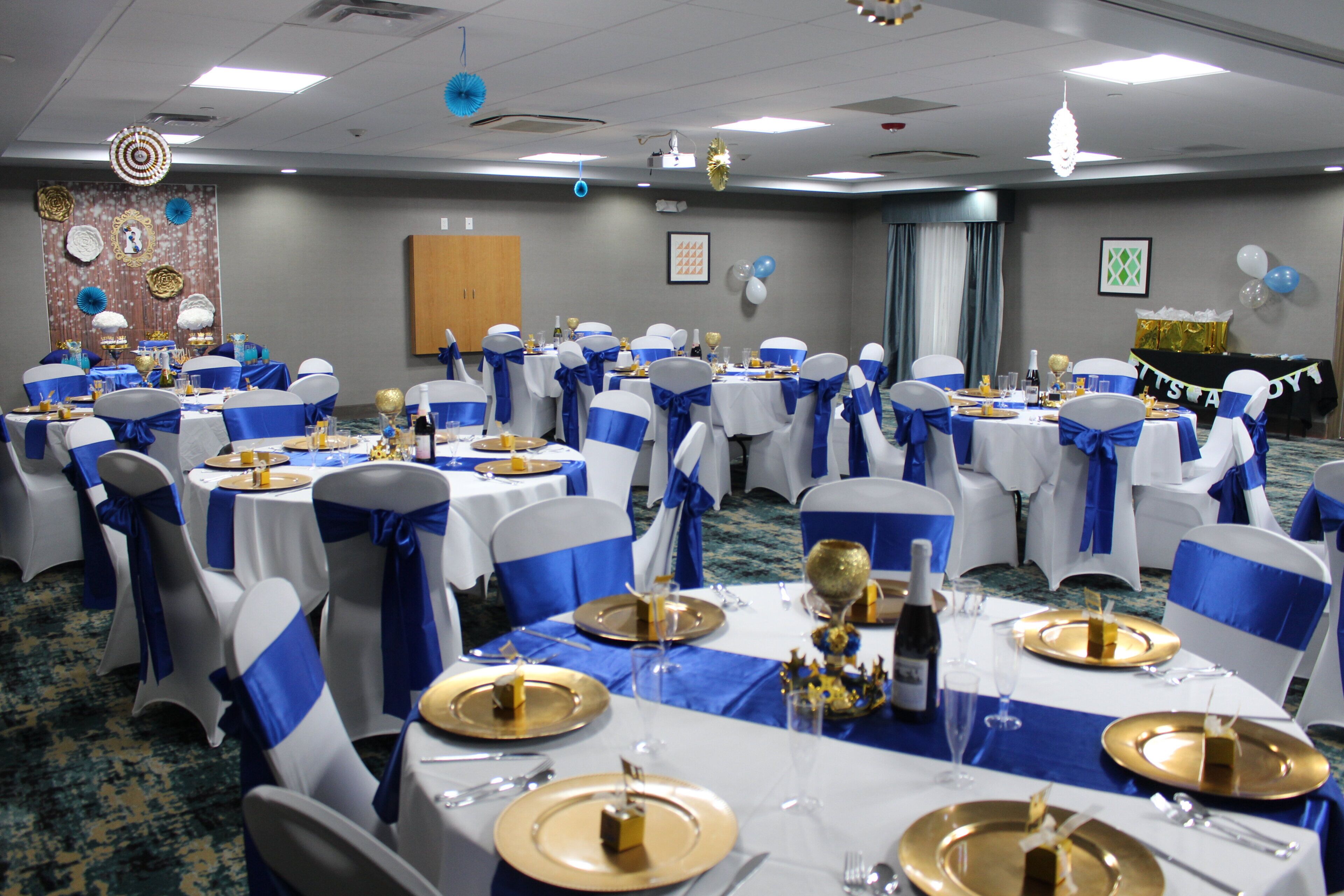 A banquet hall with round tables, chairs with blue sashes, and gold tableware.