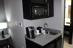 Una kitchenette compacta equipada con microondas, cafetera y lavabo.
