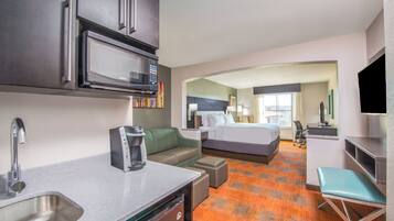 A hotel room with a kitchenette, a bed, a seating area, and a television.