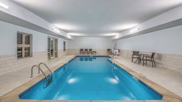 A rectangular indoor swimming pool with clear blue water, surrounded by tiled walls and a ceiling with recessed lighting.