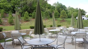 An outdoor patio area with round tables and metal chairs, surrounded by green umbrellas.