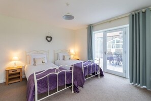 A bedroom with two beds, a nightstand, a wall-mounted heart decoration, and a sliding glass door to a balcony. - The Grainary Cottages (Scarborough)