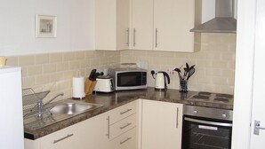 A compact kitchen with a microwave, toaster, sink, and stove. - The Grainary Cottages (Scarborough)
