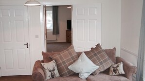 A cozy living room with a plush sofa, a hanging light fixture, and a view into an adjacent room. - The Grainary Cottages (Scarborough)