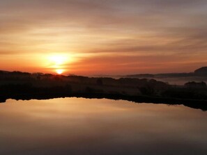 A calm body of water reflecting a sunset with a distant horizon. - The Grainary Cottages (Scarborough)