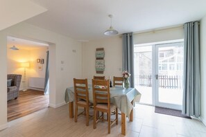 A dining area with a table set for four, wooden chairs, a hanging light fixture, and a view through a glass door to the outside. - The Grainary Cottages (Scarborough)