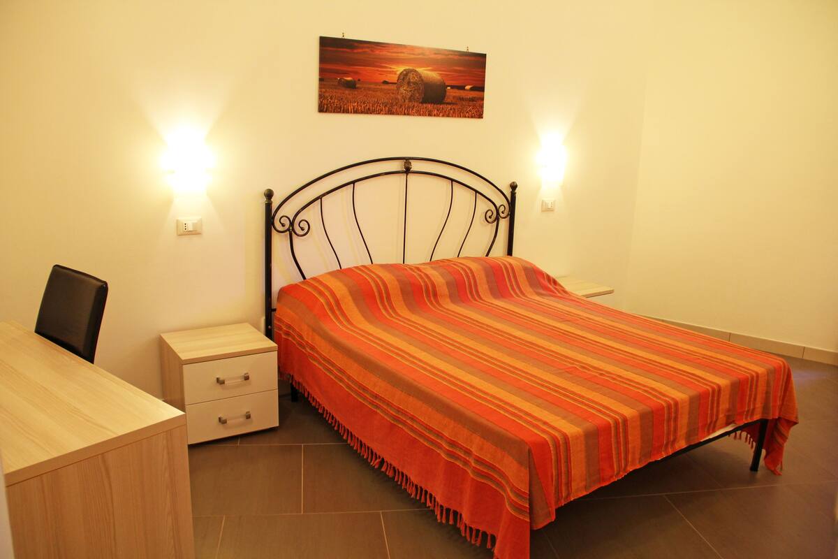 Un dormitorio ordenado con cama, mesitas de noche y un escritorio.